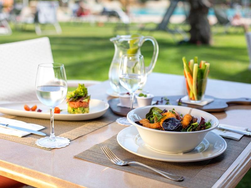 Tavolo all'aperto con insalate, bicchiere di vino bianco e brocca d'acqua in giardino.