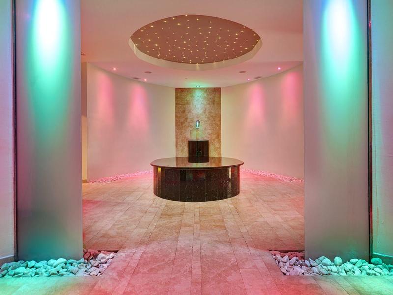 Elegante hall d'hotel con illuminazione colorata e tavolo rotondo centrale.