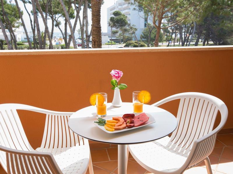 Terrazza con tavolo rotondo, due sedie bianche, bevande e dolci colorati.