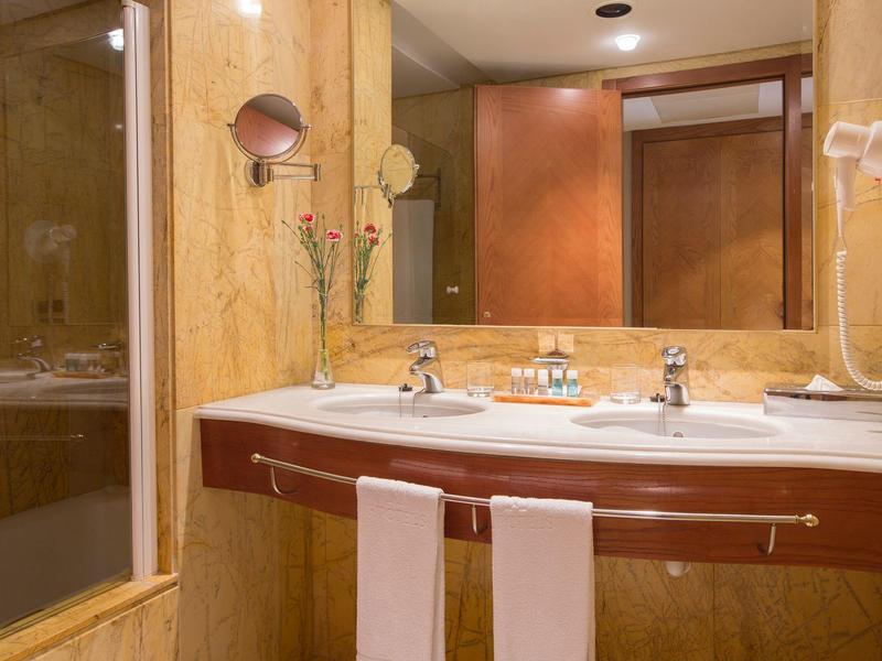 Bagno d'hotel con doppio lavabo, specchio e asciugacapelli a parete.