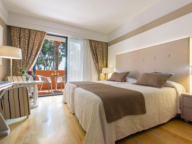 Camera d'hotel con letto matrimoniale, luce soffusa e balcone con vista sugli alberi.