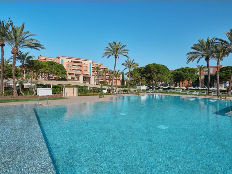 Piscina esterna azzurra chiara circondata da palme e hotel.