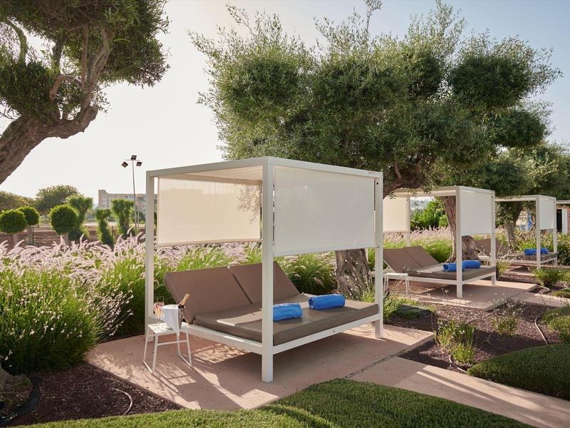Lettini moderni e confortevoli in un'area giardino di un hotel sotto gli alberi.