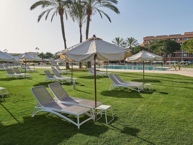 Sdraio con ombrelloni su prato verde accanto a una piscina in un resort.