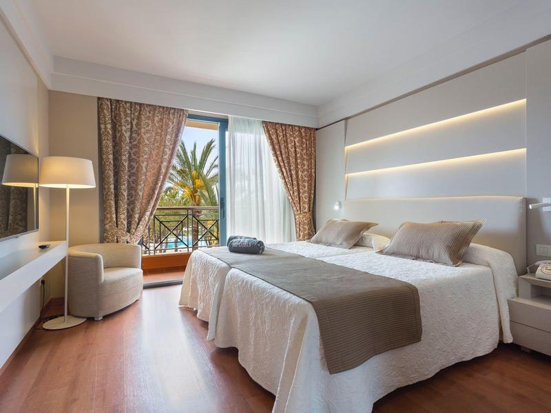 Camera d'hotel moderna con letto matrimoniale, TV a schermo piatto e balcone con vista sulle piante.