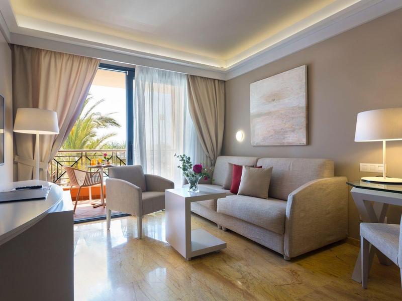 Camera d'hotel moderna con zona soggiorno e balcone con piante.