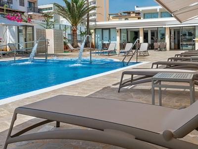 Hotelová bazénová oblast s lehátky a palmami za slunečného počasí.