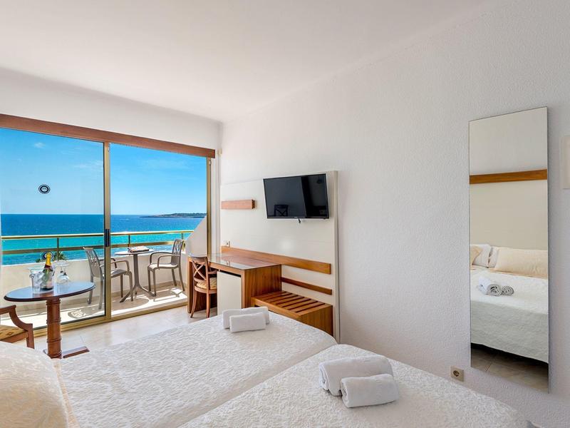 Modernes Hotelzimmer mit Doppelbett, Balkon und Meerblick bei Sonnenschein.