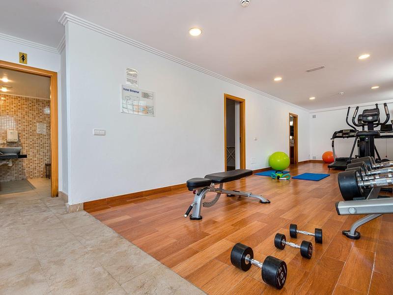 Moderner Fitnessraum mit Hanteln, Trainingsbank und Cardio-Geräten in einem Hotel.