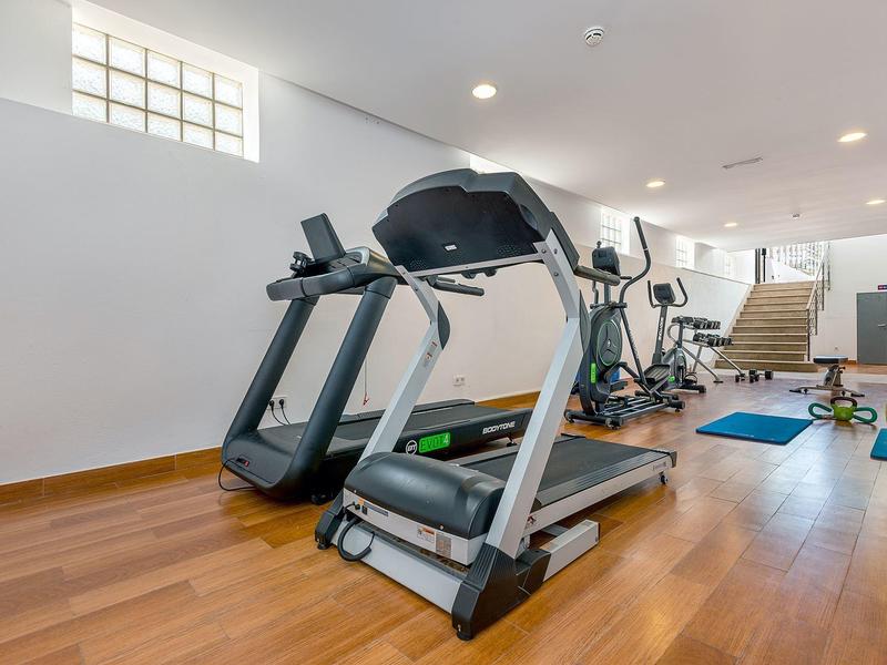 Moderner Fitnessraum mit Laufbändern, Crosstrainern und Hantelsets auf Holzboden.