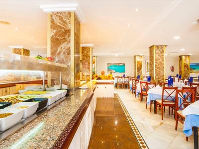 Eleganter Speisesaal mit weißen Tischen, blauen Gläsern und einem Buffet mit frischem Essen.