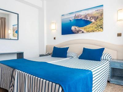 Schlafzimmer mit blau-weiß gestreiftem Bett, blauen Kissen und Decke, Wandlampe und Spiegel.