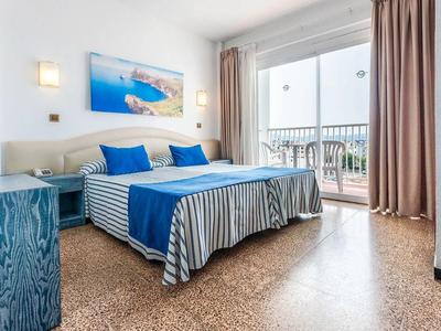 Helles Schlafzimmer mit Doppelbett, blau-weißer Bettwäsche und Balkon mit Glasgeländer.