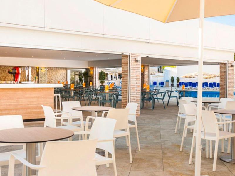 Moderner Außenbereich eines Cafés mit weißen Tischen und Stühlen, hellem Holz und Sonnenschirmen.