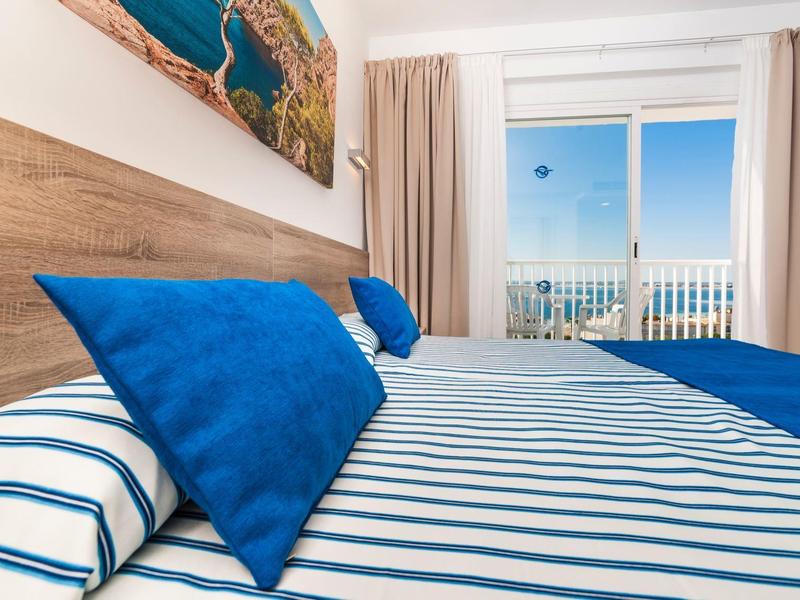 Modernes Schlafzimmer mit blau-weiß gestreiftem Bettzeug und Blick auf Meer durch großen Balkon.