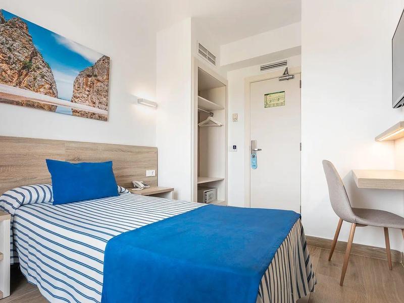 Kleines, helles Zimmer mit Einzelbett, blau-weiß gestreifter Bettwäsche und modernem Schreibtisch.