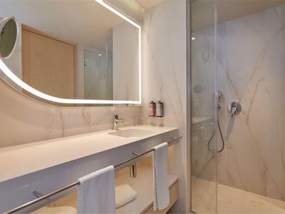 Moderne badkamer met grote verlichte spiegel, dubbele wastafel en glazen douche met marmeren wanden.