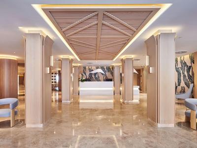 Ruime hotelhal met marmeren vloer, houten plafond, zuilen en moderne zithoeken.