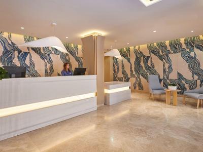 Moderne hotelreceptie met marmeren vloer, witte balies en muren met abstract patroon.
