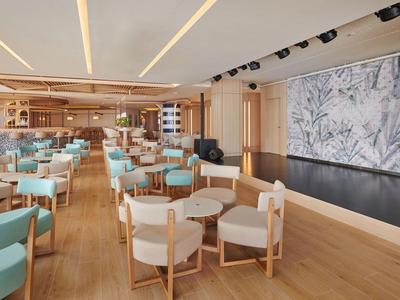 Ruime hotel eetruimte met houten vloeren, lichtblauwe en beige stoelen en grote botanische wanddecoratie.