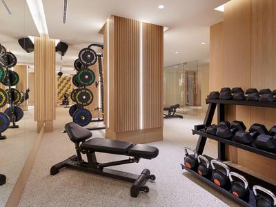 Nowoczesna siłownia z hantlami, ciężarami i ławką treningową w jasnym otoczeniu.