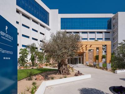 Modern hotelgebouw met aangelegde tuin en heldere blauwe lucht.