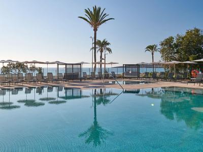 Zwembad met palmbomen en ligstoelen nabij de oceaan bij een resort.