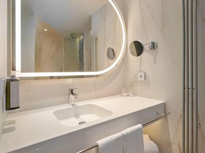 Moderne hotelbadkamer met grote verlichte spiegel en wit aanrecht.