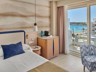 Hotelkamer met bed, stoel, minibar en balkon met uitzicht op zee.