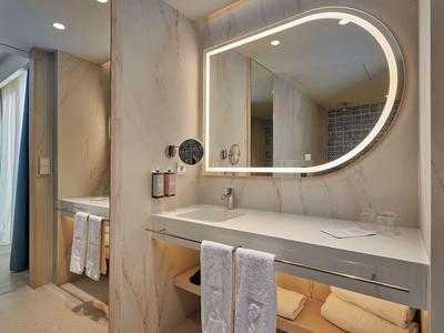 Moderne hotelbadkamer met verlicht ovale spiegel, dubbele wastafel en netjes opgevouwen handdoeken.