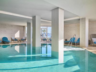 Modern binnenzwembad met zuilen, ligstoelen en grote ramen.