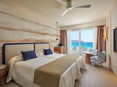 Lichte hotelkamer met twee eenpersoonsbedden en zeezicht door de ramen.