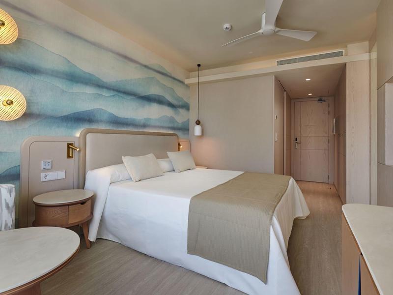 Moderne hotelkamer met tweepersoonsbed, blauwe golfmuur, beige inrichting en minimalistisch meubilair.