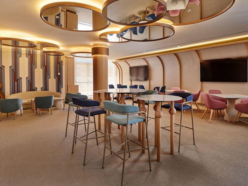 Moderne lounge met hoge tafels, kleurrijke stoelen en warme verlichting in een luxe hotel.