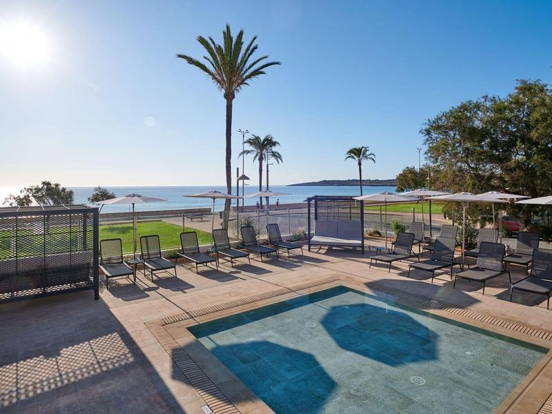 Buitenzwembad met ligstoelen en parasols met uitzicht op de oceaan en palmbomen.
