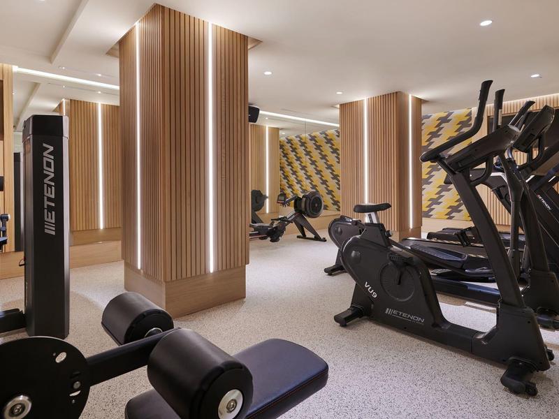 Moderne hotelgym met cardio- en krachtapparaten, houten panelen en heldere verlichting.