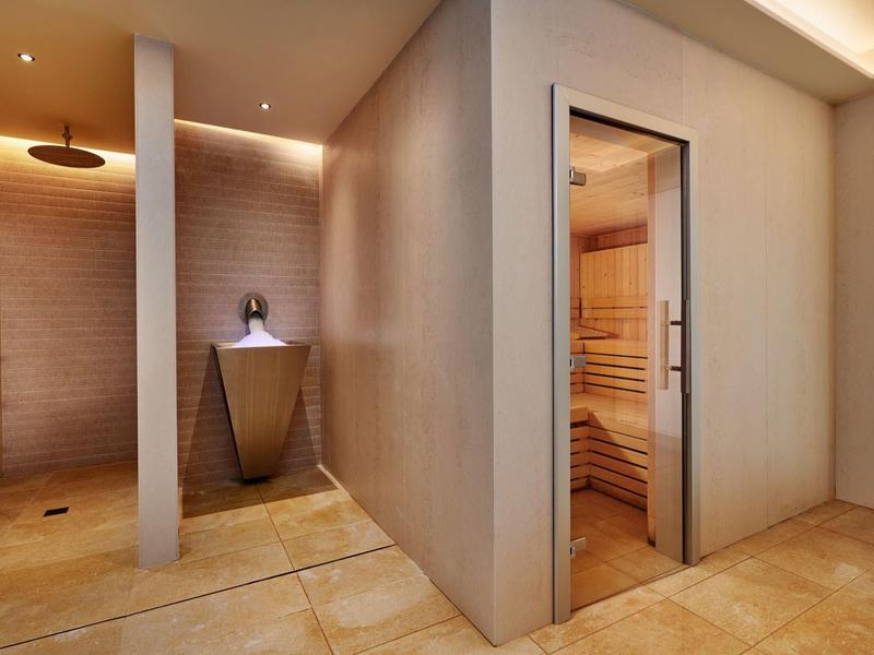 Moderne spa met saunaruimte en douche, warme verlichting, beige muren en betegelde vloer.