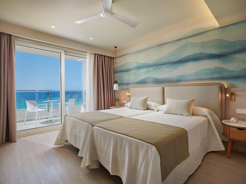 Hotelkamer met twee eenpersoonsbedden, balkon met uitzicht op zee en lichte, luchtige inrichting.