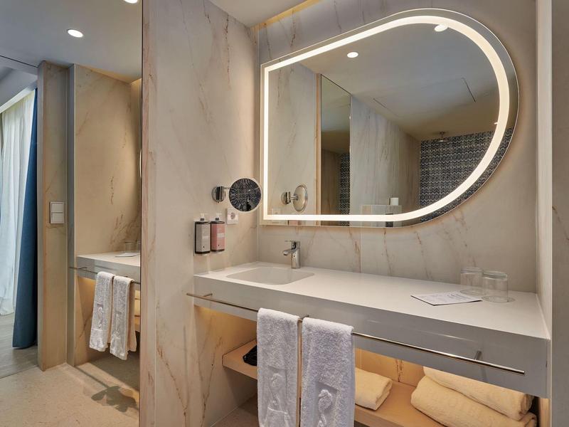 Moderne hotelbadkamer met verlicht ovale spiegel, dubbele wastafel en netjes opgevouwen handdoeken.