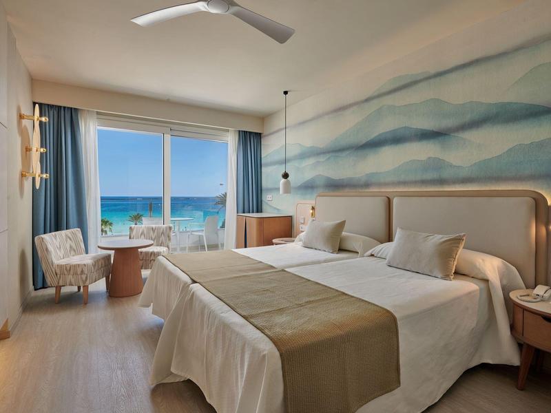 Lichte hotelkamer met tweepersoonsbed, zeezicht, modern interieur en lichte houten vloer.