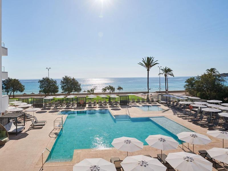 Hotelzwembad met zonneschermen en uitzicht op zee onder heldere lucht.