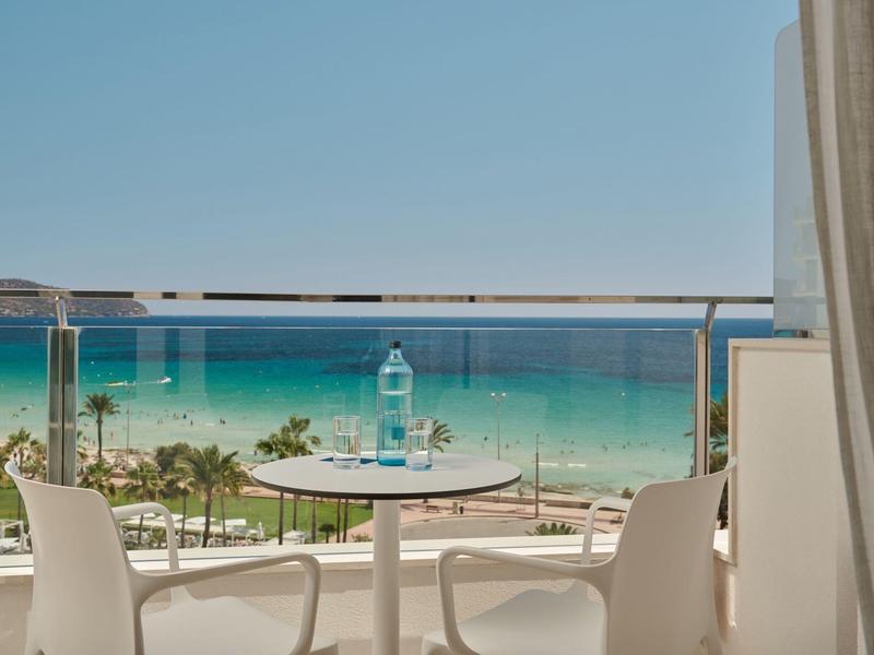 Uitzicht vanaf balkon met tafel en stoelen op zee en strand onder een heldere hemel.