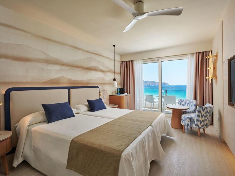 Lichte hotelkamer met twee eenpersoonsbedden en zeezicht door de ramen.