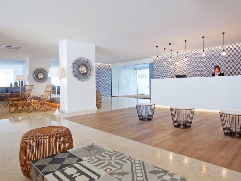 Lichte hotellobby met moderne receptie, houten vloer en zitgedeelte met patroon kussens.