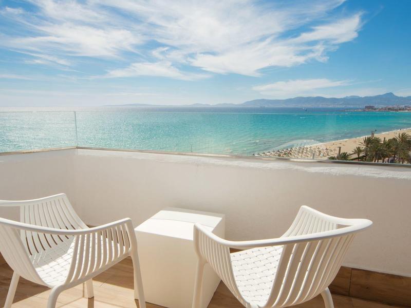 Balkon met witte stoelen en tafel met uitzicht op zee en strand.
