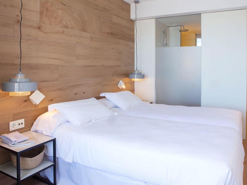 Modern hotelkamer met tweepersoonsbed, houten wand, nachtkastje en hanglampen.