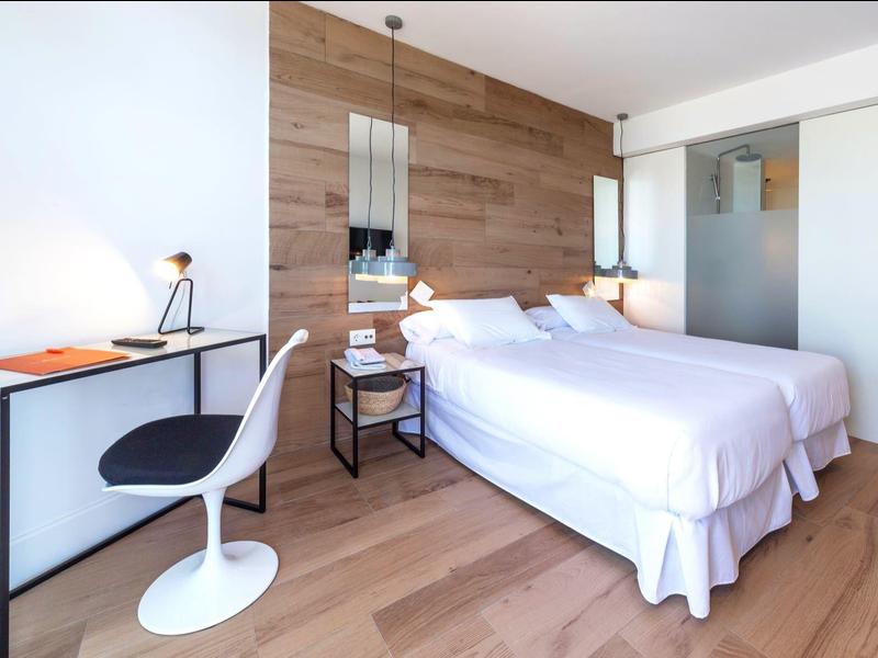 Modern hotelkamer met twee bedden, houten vloer en bureau met stoel.