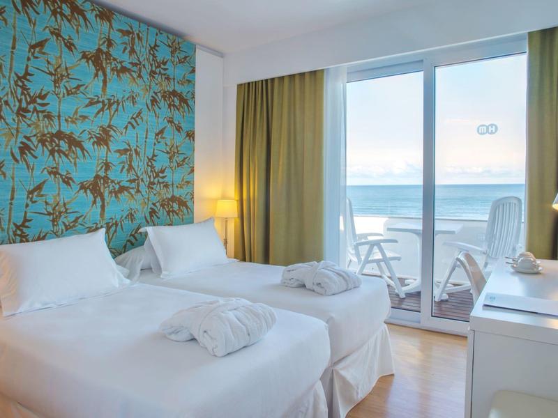 Lichte hotelkamer met twee eenpersoonsbedden, zeezicht en balkon.