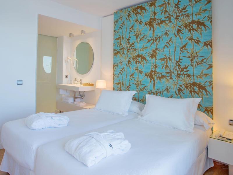 Moderne hotelkamer met twee eenpersoonsbedden, blauwe bloemenmuur en witte badjassen.