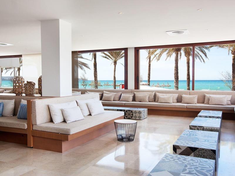 Lichte hotel lounge met grote ramen, zeezicht en modern houten meubilair.